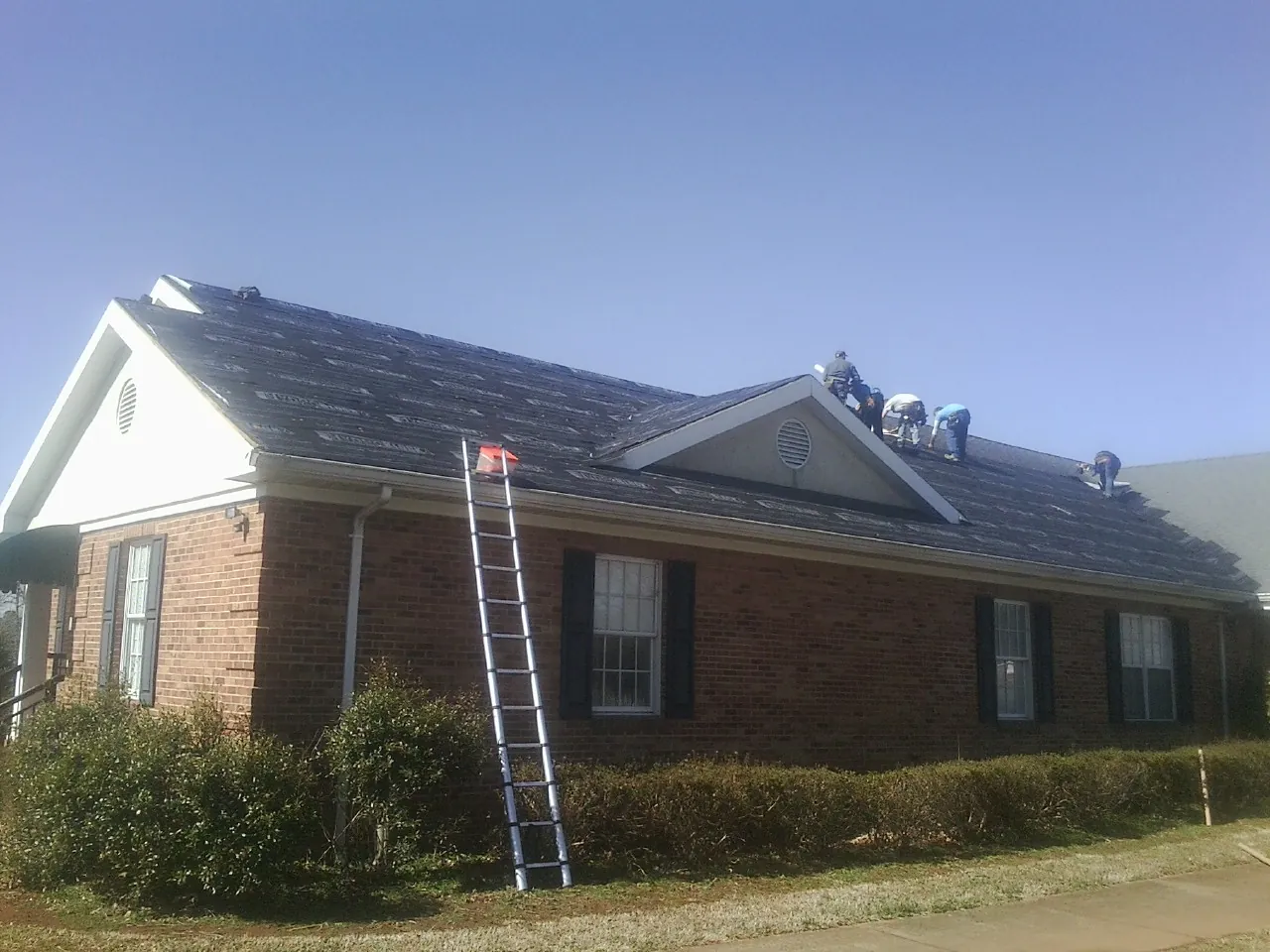 Crew tearing shingles off a brick ranch roof with a ladder set — Emergency Roof Repair work by our crew in Malaga