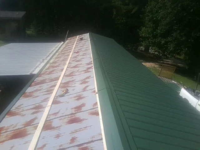 Old rusted panels beside newly installed green metal roofing — Wind Damage Roof Repair by Roofing Brothers in Malaga