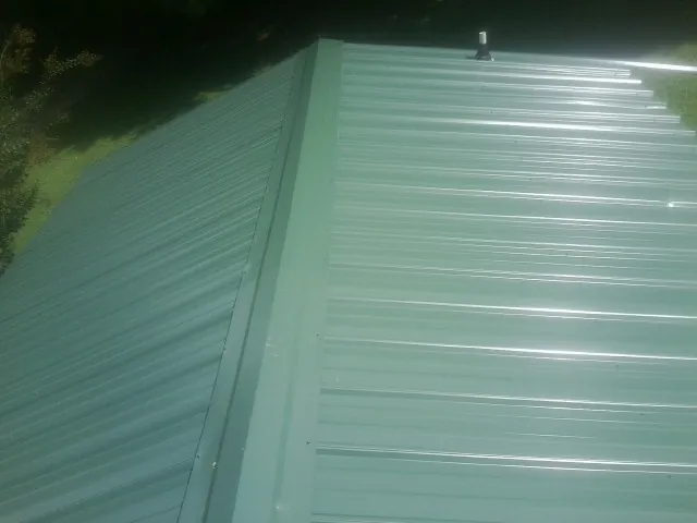 New green metal panels meeting at the ridge of a roof — Flat Roof Repair work by our crew in Malaga