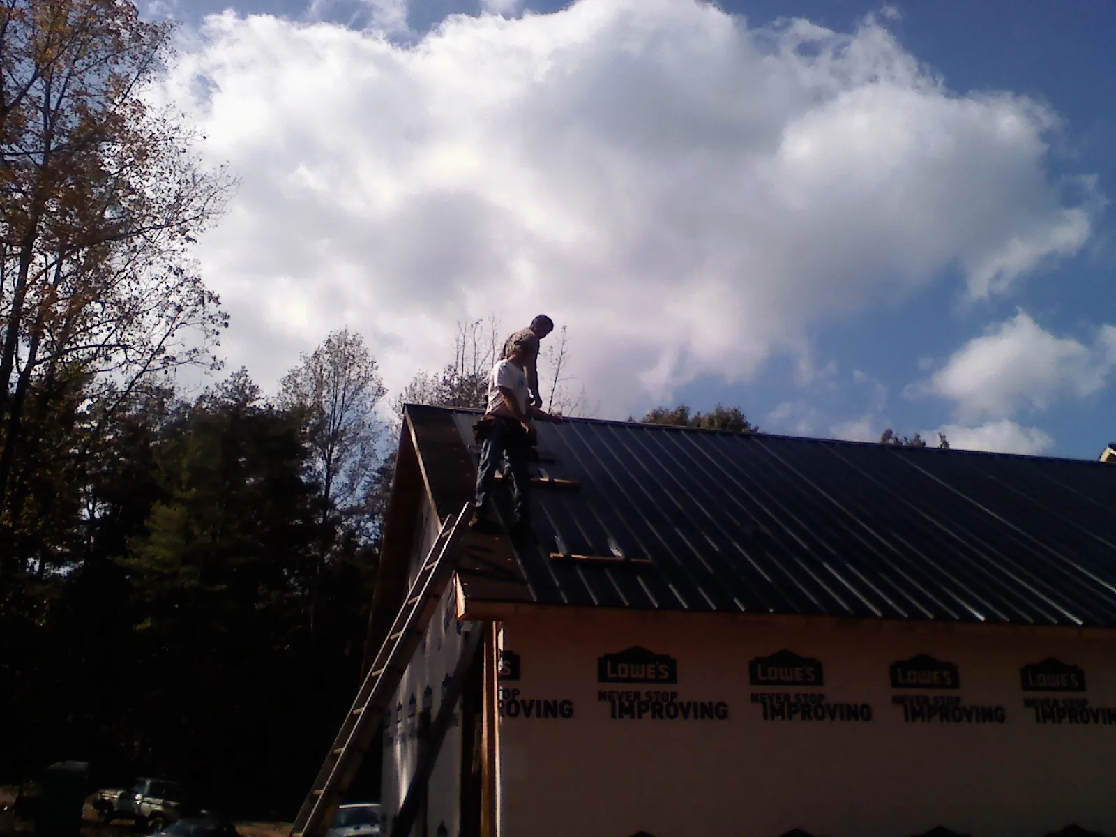 Roofer fastening dark metal panels high against a cloudy sky, from a Roof Inspection job in Malaga