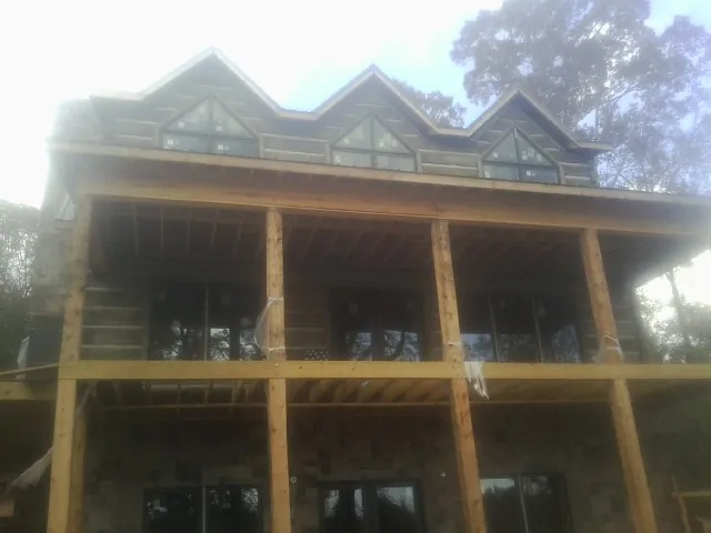 Dormers and porch framing on a large log home under construction — Roof Coating work by our crew in Malaga