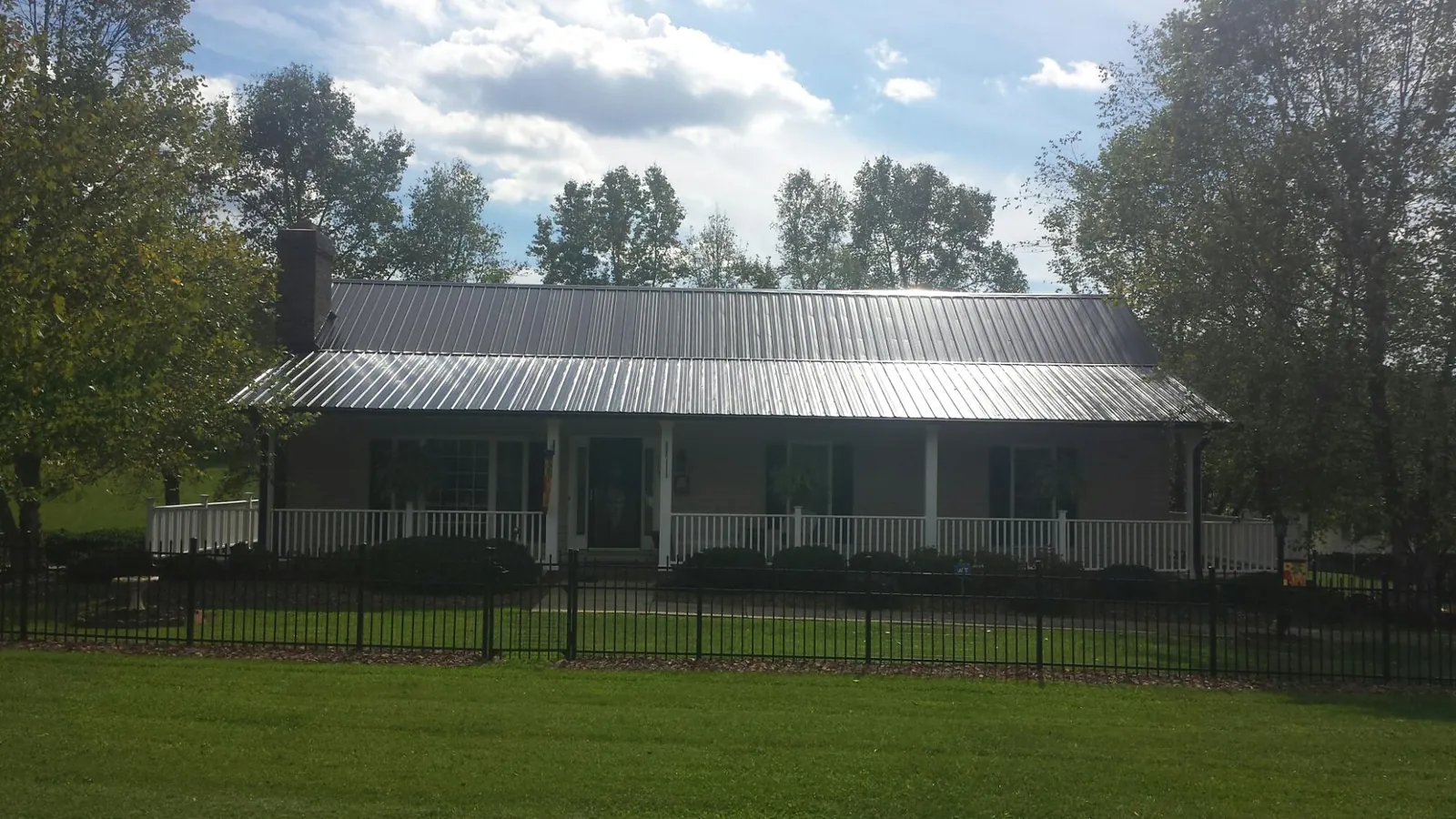 Gray metal roof on a brick ranch with a full width front porch — Gutter Guard Installation work by our crew in Malaga